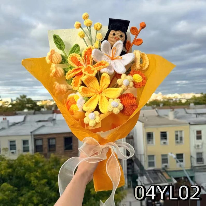 Crochet graduation bouquet in orange and yellow shades with lily-shaped crochet flowers, accented with golden ribbon.