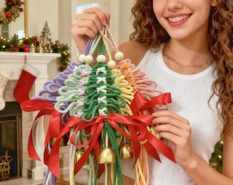 Op de afbeelding: Een kleurrijke macramé kerstboomversiering met een regenboog van pastelkleuren, houten kralen en gouden bellen. De boom is versierd met rode satijnen linten. Een feestelijke vakantieversiering.