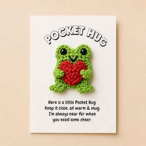 Op de afbeelding: Een kleine gehaakte groene kikker die een rood gehaakt hart vasthoudt, bevestigd op een witte kaart. De kaart bevat de tekst POCKET HUG bovenaan en een gedicht eronder: Here is a little Pocket Hug. Keep it close, all warm & snug. I'm always near for when you need some cheer.