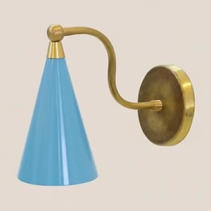 Puede incluir: Lámpara de pared con una pantalla cónica azul claro y un brazo curvo de latón. La lámpara tiene una base redonda de latón y un acento de latón en la parte superior de la pantalla. El diseño es retro y elegante.