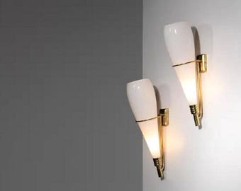 Könnte beinhalten: Zwei Wandleuchten mit weißem, tropfenförmigem Glasschirm und goldfarbenen Metallakzenten. Die Leuchten sind an einer weißen Wand montiert, mit einer grauen Wand im Hintergrund.