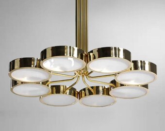 May include: A gold-toned chandelier with eight circular light fixtures. Each fixture has a gold rim and a white, opaque center. The chandelier is suspended from a central gold rod.