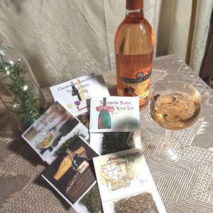 May include: A set of six wine dip mixes with different flavors, including Rose' Holiday, Chardonnay Sun-dried Tomato Pesto, Sauvignon Blanc Cheese, and Riesling Ginger. The mixes are packaged in clear plastic bags with labels and are displayed on a table with a bottle of wine and a glass of wine.
