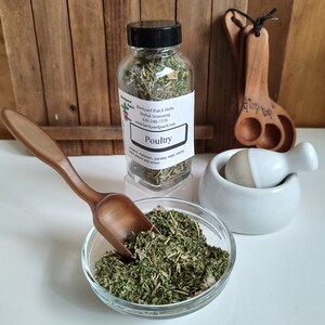 Pu&ograve; includere: Un barattolo di vetro pieno di erbe secche etichettato "Poultry" con il testo "Backyard Patch Herbs" e "www.backyardpatch.com". Il barattolo &egrave; su una superficie di legno accanto a un piccolo mortaio e pestello bianco e una paletta di legno.