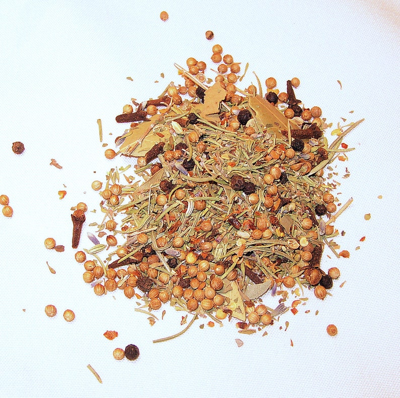 May include: A close-up of a mixture of dried herbs and spices, including bay leaves, peppercorns, and coriander seeds. The mixture is scattered on a white surface.
