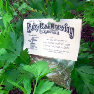 May include: A white label with the text "Salt-Free Ruby Rea Dressing Backyard Patch" and a description of the ingredients. The label is sitting on a bed of green parsley.