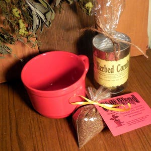 May include: A red ceramic mug, a clear glass jar with a yellow label that reads "Herbed Cornbread" and a small bag of brown seeds with a yellow label that reads "Chili Blend" and a yellow ribbon.