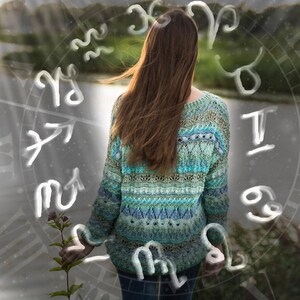May include: A woman with long brown hair wearing a blue and green patterned sweater stands in front of a blurred background with white zodiac symbols.