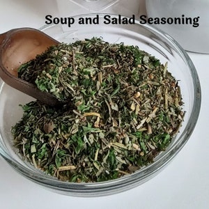 May include: A glass bowl filled with a blend of dried herbs and spices, labeled "Soup and Salad Seasoning".