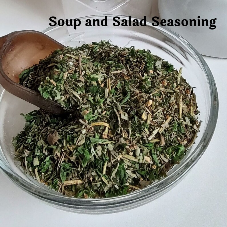 May include: A glass bowl filled with a blend of dried herbs and spices, labeled "Soup and Salad Seasoning".