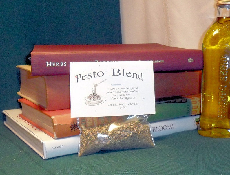 May include: A clear plastic bag filled with dried herbs labeled "Pesto Blend". The bag is sitting on top of a stack of books. The label says "Create a marvelous pesto flavor when fresh basil or time eludes you. Wonderful on pasta! Contains basil, parsley and garlic."