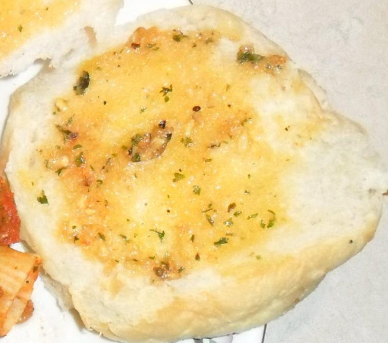 Peut inclure: Gros plan sur un pain rond blanc garni de beurre fondu et d'herbes. Le pain est l&eacute;g&egrave;rement dor&eacute; et a une texture croustillante.