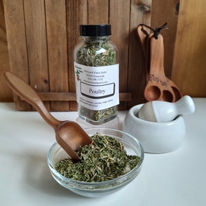 Pu&ograve; includere: Un barattolo di vetro pieno di erbe secche etichettato "Poultry" con i seguenti ingredienti: "coriandolo, maggiorana, prezzemolo, salvia, santoreggia, pepe nero e cipolla". Il barattolo &egrave; su una superficie di legno con un cucchiaio di legno e un mortaio e un pestello bianchi.