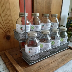 May include: A metal rack with eight glass jars filled with herbs and spices. The jars have labels that say "Backyard Patch" and list the herbs and spices inside. The rack is on a wooden surface.