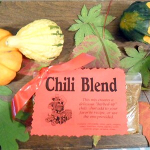 May include: A red and white label with the text "Chili Blend" on it. The label is tied with a red ribbon and is sitting on a wooden surface with gourds and fall leaves.
