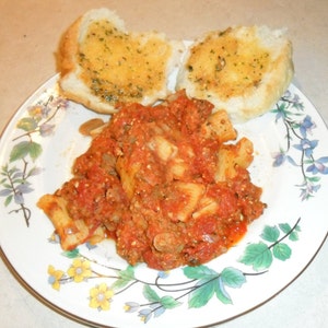 Peut inclure: Une assiette blanche &agrave; motif floral pr&eacute;sente une portion de p&acirc;tes &agrave; la sauce rouge et &agrave; la viande hach&eacute;e. Deux morceaux de pain &agrave; l'ail sont sur le c&ocirc;t&eacute;.