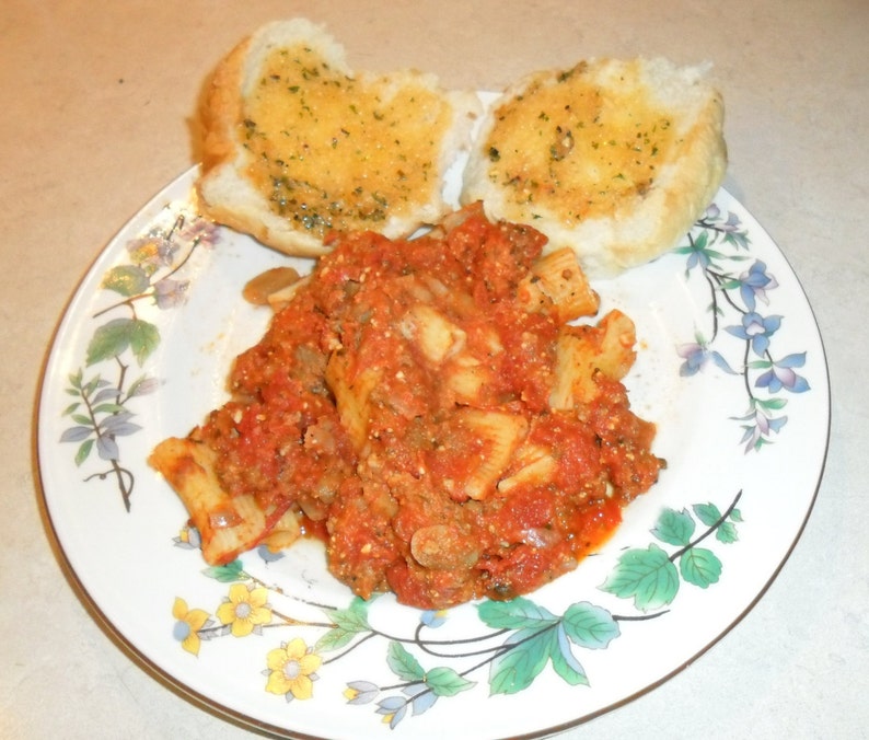 Peut inclure: Une assiette blanche &agrave; motif floral pr&eacute;sente une portion de p&acirc;tes &agrave; la sauce rouge et &agrave; la viande hach&eacute;e. Deux morceaux de pain &agrave; l'ail sont sur le c&ocirc;t&eacute;.