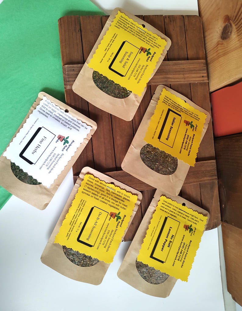 May include: Four small brown paper bags with yellow labels containing dried herbs. The labels have the name of the herb blend, "Fine Herbs", "Italian Seasoning", "Soup & Salad Seasoning", and "Do-It-All Seasoning".