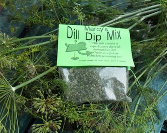 Peut inclure: Un sachet vert et blanc de mélange à trempette à l'aneth de Marcy. Le sachet est posé sur un lit d'aneth frais. Le texte sur le sachet indique "Marcy's Dill Dip Mix" et "Ce mélange crée une trempette de fête exceptionnelle avec de l'aneth cultivé à la maison. Excellent comme assaisonnement pour le poisson ou le poulet aussi ! Contient du persil, de l'aneth, de l'oignon, de la ciboulette, du cerfeuil et du tarragon."