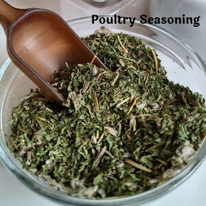 May include: A glass bowl filled with dried herbs and spices, labeled "Poultry Seasoning". A brown wooden scoop is partially in the bowl.