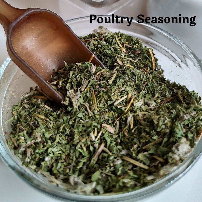 May include: A glass bowl filled with dried herbs and spices, labeled "Poultry Seasoning". A brown wooden scoop is partially in the bowl.