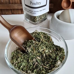 Pu&ograve; includere: Un barattolo di vetro pieno di erbe secche etichettato "Poultry" con il testo "Backyard Patch Herbs, Herbal Seasoning, 630-248-7278, www.backyardpatch.com". Il barattolo &egrave; su una superficie di legno. Il barattolo contiene maggiorana, prezzemolo, salvia, santoreggia, pepe nero e cipolla.
