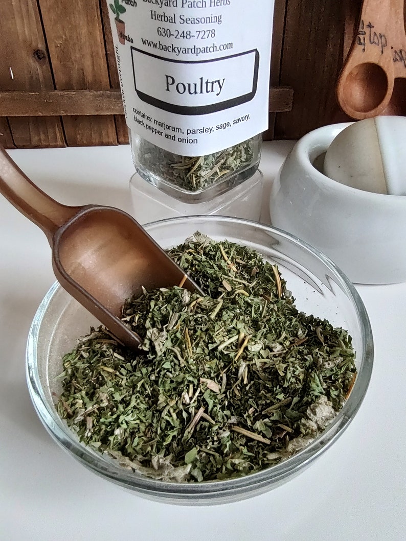 Pu&ograve; includere: Un barattolo di vetro pieno di erbe secche etichettato "Poultry" con il testo "Backyard Patch Herbs, Herbal Seasoning, 630-248-7278, www.backyardpatch.com". Il barattolo &egrave; su una superficie di legno. Il barattolo contiene maggiorana, prezzemolo, salvia, santoreggia, pepe nero e cipolla.