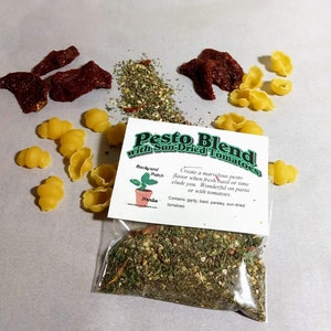 May include: A clear plastic bag filled with a pesto blend with sun-dried tomatoes. The bag has a label that reads "Pesto Blend with Sun-Dried Tomatoes". The label also includes the text "Backyard Patch Herba" and "Create a marvelous pesto flavor when fresh basil or time elude you. Wonderful on pasta or with tomatoes. Contains: garlic, basil, parsley, sun-dried tomatoes."