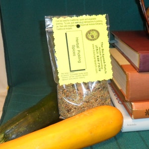 May include: A yellow and green package of Herbal Pickling Spices from The Backyard Patch. The package is sitting on a stack of books. The text on the package reads "Herbal Pickling Spices" and "The Backyard Patch Herbal Seasoning (630) 248-7978 www.backyardpatch.com".