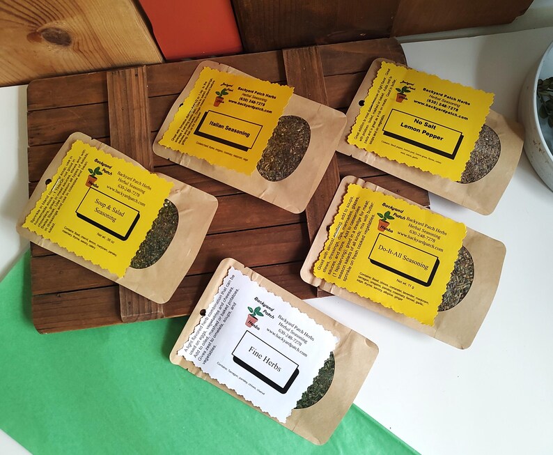 May include: Five brown paper bags with yellow labels containing different types of dried herbs and spices. The labels have the name of the blend, "Backyard Patch Herbs", and a website address. The blends are "Soup & Salad Seasoning", "Italian Seasoning", "No Salt Lemon Pepper", "Do-It-All Seasoning", and "Fine Herbs".