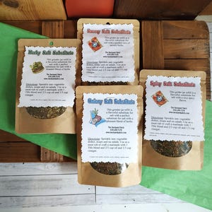 May include: Four brown paper pouches with labels for different salt substitutes: Herby, Savory, Oniony, and Spicy. Each pouch contains a blend of herbs and spices. The labels include the name of the product, a description, directions for use, and contact information for The Backyard Patch.