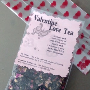 May include: A pink and white Valentine's Day tea bag with a heart design. The tea bag contains a blend of black tea, rose petals, and chocolate. The text on the bag reads "Valentine Love Tea" and includes brewing instructions.