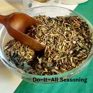 May include: A glass bowl filled with a blend of dried herbs and spices, labeled "Do-It-All Seasoning". A wooden scoop is partially submerged in the bowl.