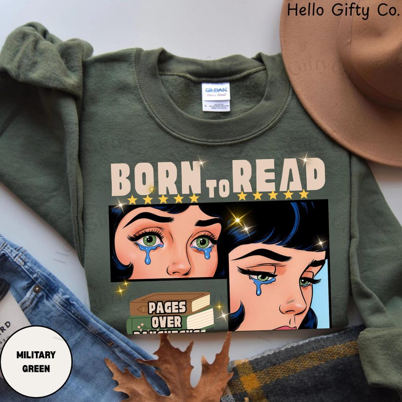 May include: Military green sweatshirt with the text "BORN TO READ" above a graphic of a crying woman. The graphic includes the text "PAGES OVER DAUGHTERS". The sweatshirt is a Gildan brand.