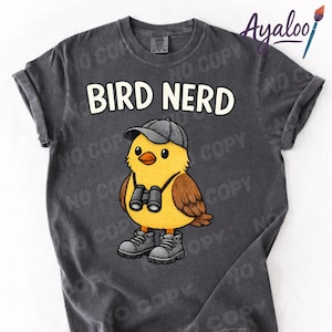Op de afbeelding: Donkergrijs t-shirt met de tekst "BIRD NERD" boven een cartoonvogel met een pet, een verrekijker en laarzen. De vogel is geel met bruine vleugels.