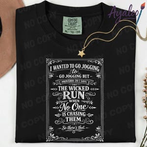 May include: Black t-shirt with a humorous quote in white script: "I WANTED TO GO JOGGING to GO JOGGING BUT - PROVERBS 28:1 SAYS THE WICKED RUN when No One IS CHASING THEM. - So there's that." A gold necklace with a star pendant is draped on the shirt.