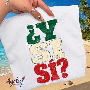 Può includere: Una t-shirt bianca con il testo ¿Y SI SÍ? stampato in un carattere usurato e screpolato. Le lettere sono colorate in verde, bianco sporco e rosso, disposte verticalmente su tre righe. Il design presenta un aspetto invecchiato e vintage.