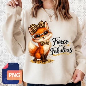 May include: A beige sweatshirt featuring a cartoon fox with a bow, glasses, and bow tie, all with a leopard print design. The text "Fierce and Fabulous" is written in black script. The fox is sitting on a leopard print pattern.