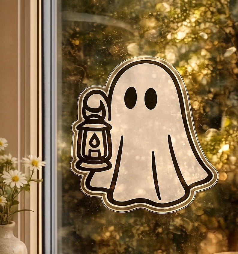 May include: A white ghost-shaped sticker with a black outline and holding a lantern. The ghost has two black oval eyes and a simple, friendly design. The sticker is likely for Halloween decorations.