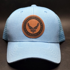 Op de afbeelding: Lichtblauwe baseballcap met een mesh achterkant en een gebogen klep. De cap heeft een bruine leren patch met de woorden "United States Air Force" en het Air Force-embleem.