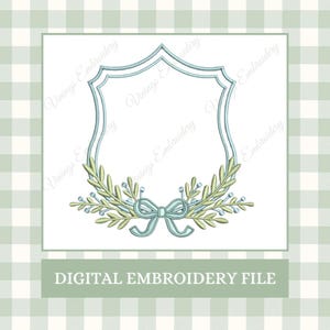 Op de afbeelding: Digitaal borduurbestand met een schildvormig frame met een lichtblauwe omtrek. Het frame is versierd met groene bladeren, blauwe bessen en een lichtblauwe strik. De tekst "DIGITAL EMBROIDERY FILE" staat onderaan.