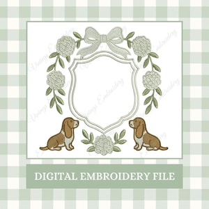 May include: Digital embroidery file featuring a shield design with a bow, floral accents, and two brown and white basset hounds. The text "DIGITAL EMBROIDERY FILE" is at the bottom. The design is on a white background with a green gingham pattern.