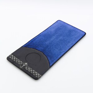 Puede incluir: Un tarjetero rectangular con una superficie azul texturizada y una base negra. La base negra presenta un diseño circular y un patrón decorativo en el borde. El tarjetero está sobre un fondo blanco.