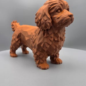 May include: A brown, geometric-style dog figurine. The sculpture has a textured surface and is posed in a standing position. The dog's fur, ears, and tail are detailed with angular facets, giving it a modern, artistic look. The figurine is set against a neutral background.
