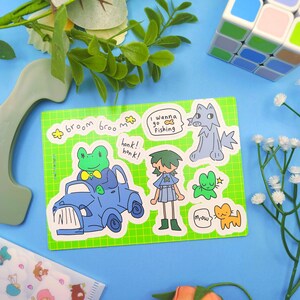 May include: A sticker sheet with cartoon illustrations of various characters. The stickers include a frog in a blue car, a wolf, a person, a cat, and other creatures. Text includes "broom broom", "honk honk", "I wanna go fishing", and "mrow".