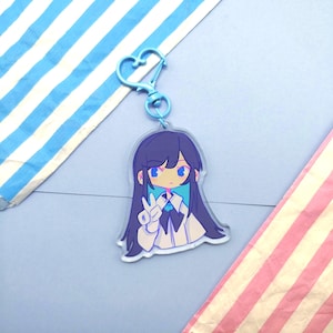 May include: A clear acrylic keychain featuring an anime-style girl with long dark blue hair and blue eyes. The girl is wearing a white shirt and making a peace sign. The keychain has a light blue heart-shaped clasp.