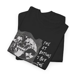 Könnte beinhalten: Schwarze T-Shirts mit einem grafischen Design. Das Design zeigt ein Schwarz-Weiß-Bild einer Person und den Text "BROADCAST BUTTONS" und "THE AT BUTTON'S BOY THE". Die Hemden sind gefaltet.