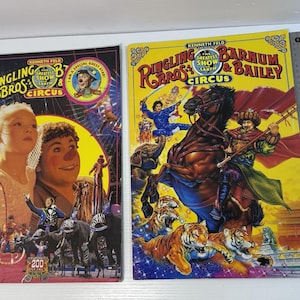 May include: Two Ringling Bros. and Barnum & Bailey Circus programs. The left program features a child and clown with circus performers. The right program shows a rider on a horse with tigers and elephants. A 16-inch metal ruler is placed on the right.