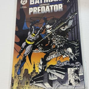 May include: A Batman Versus Predator comic book, issue 1 of 3, featuring a cover illustration of Batman in a blue and grey suit fighting the Predator character. The background shows a city skyline at sunset with orange and yellow gradients.