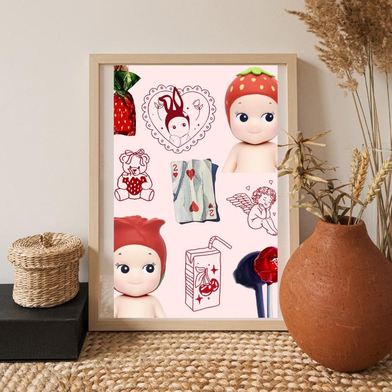 May include: A framed print featuring a light pink background with various illustrations and two doll figures. Illustrations include a strawberry-wrapped candy, a heart-shaped design with a bunny, a teddy bear, a playing card, an angel, and a juice box. The dolls wear strawberry and rose-shaped hats.